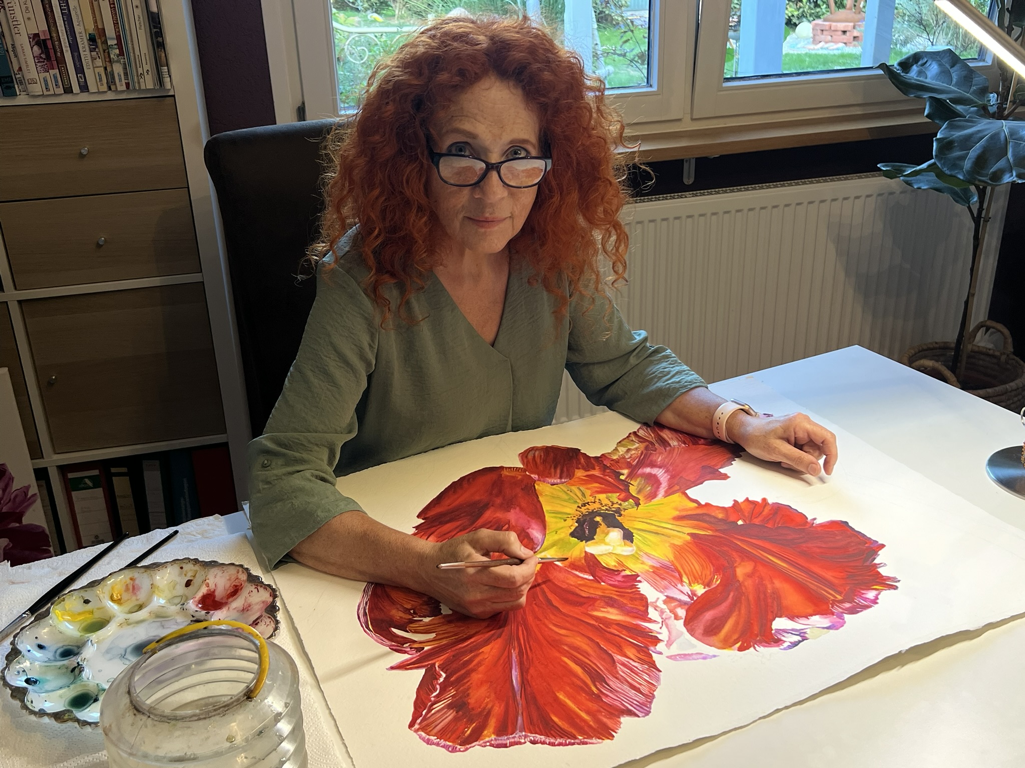 Doris Joa malt eine große rote Blume in Aquarell und blickt in die Kamera
