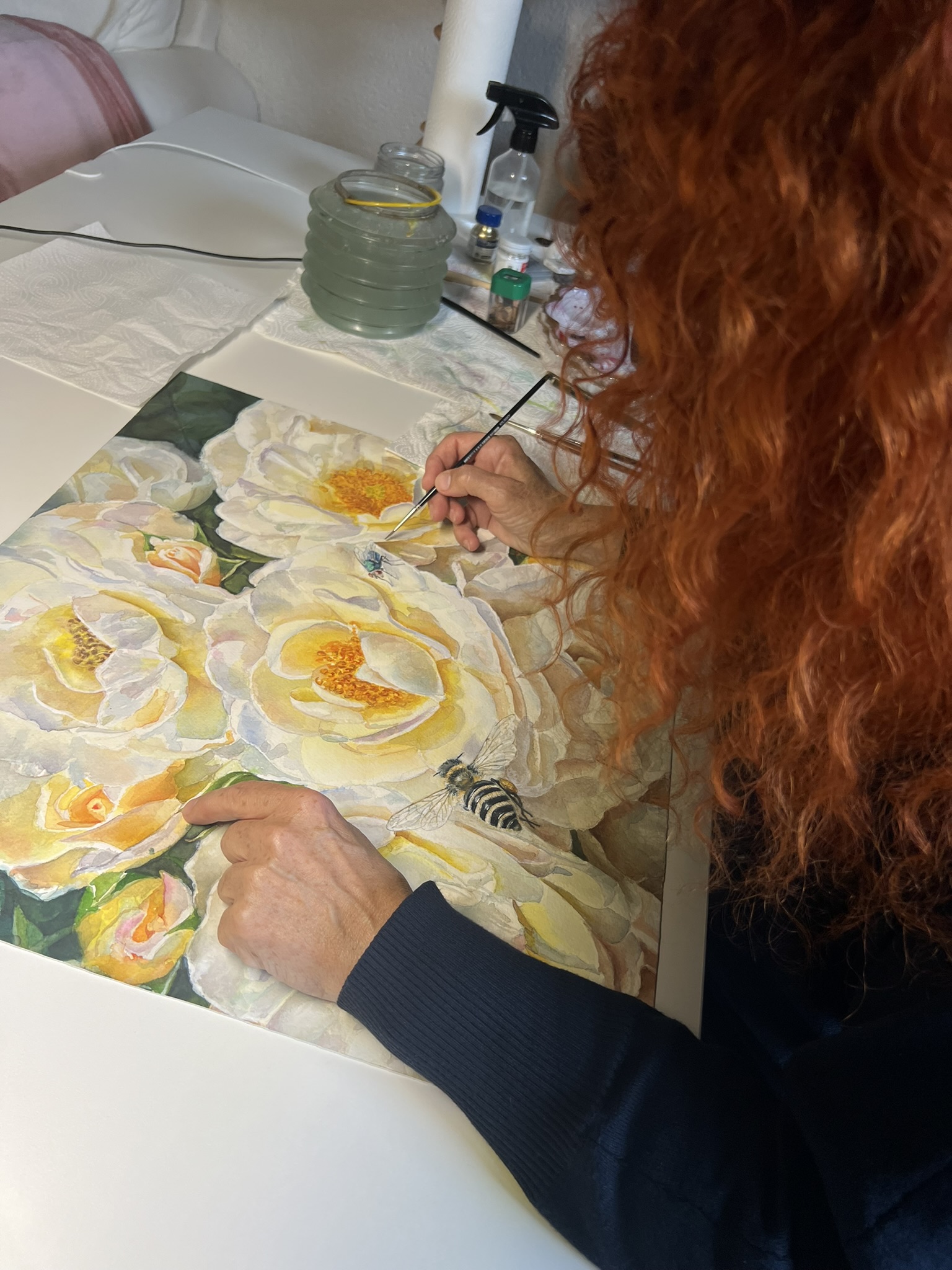 Side view of Doris Joa working on her original white rose watercolor with a bee and a fly